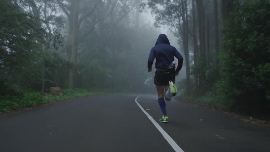 Following a jogger running up a road through the forest surrounded by mist