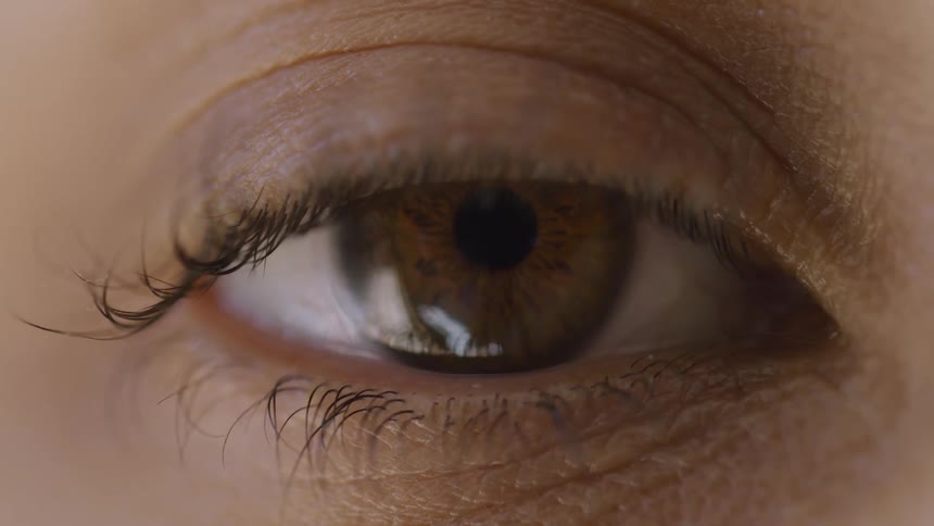 A womans eye is closed and she opens her eyelid and looks out with a brown eye