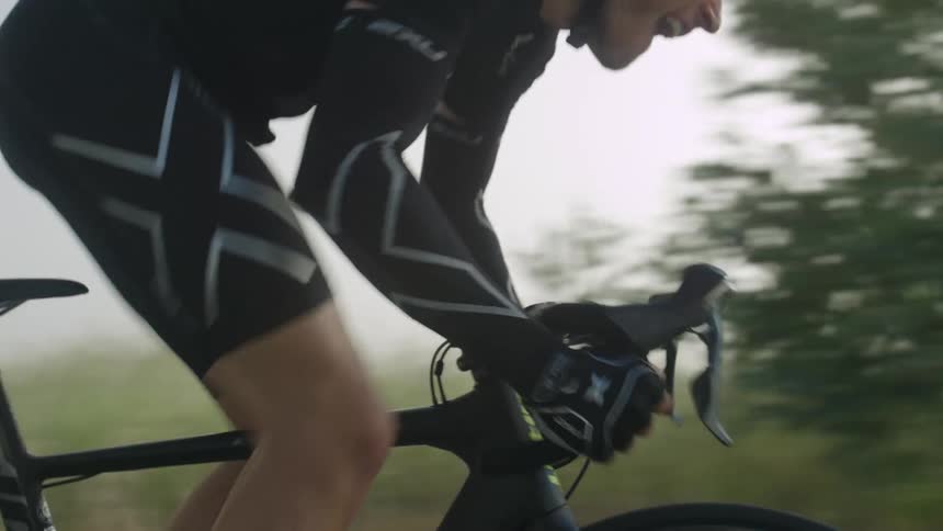 A man energetically pedals a bicycle on a road through the countryside at morning