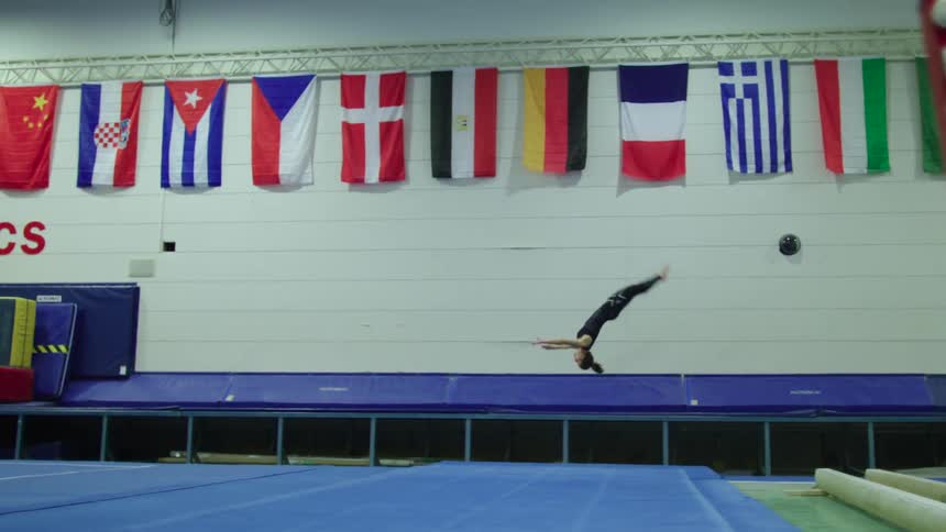 A young woman doing back flips on a trampoline in a gym as part of the warming up routine for an international gymnastics competition