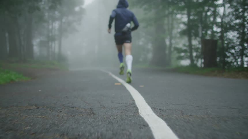 The back of a man in shorts with defined calf muscles running on an empty foggy road