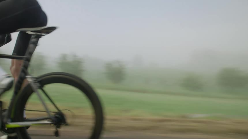 Male cyclist pedals quickly along road through countryside on foggy day
