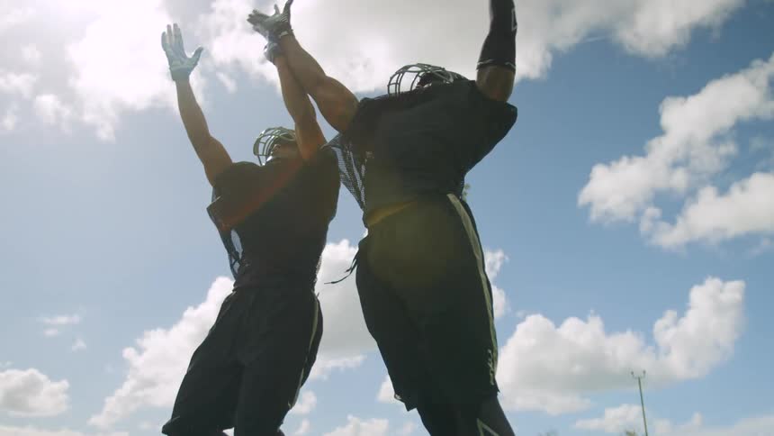 Two football players jump to catch a ball in the end zone