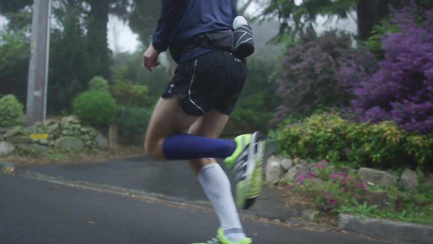Following a jogger running up a road near a forest surrounded by mist