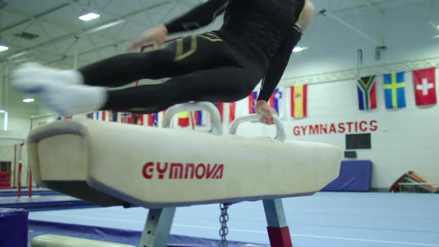 Gymnast in black jersey shirt and pants performs on pommel horse