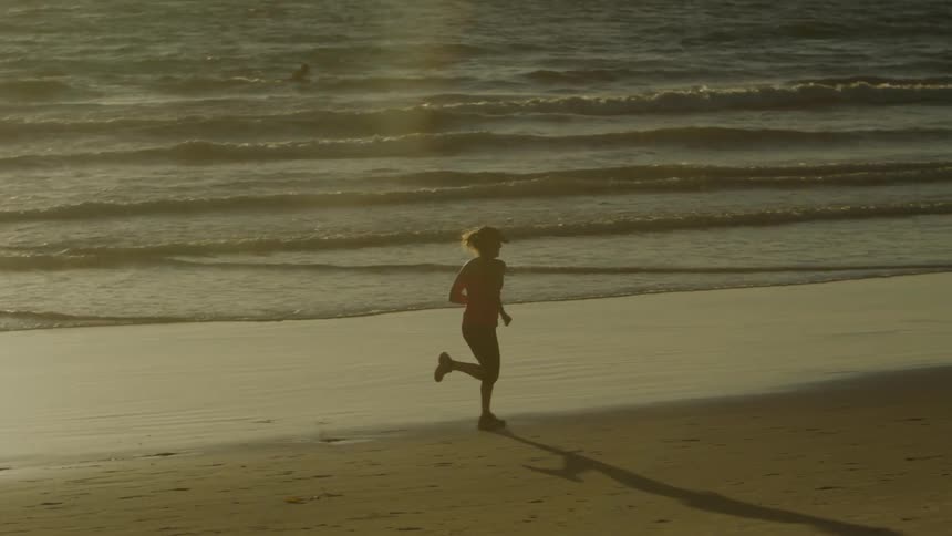 Woman jogs along beach as waves roll onto shore