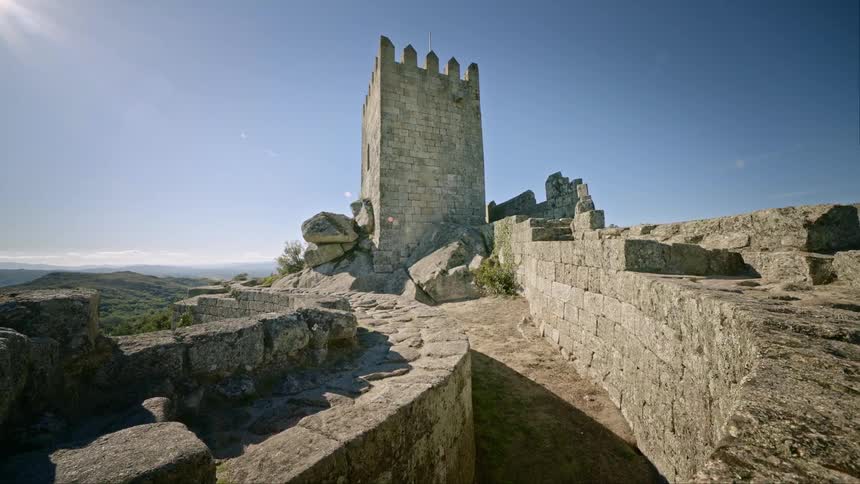 An old castle and wall sit on top of a mountain under a clear sky