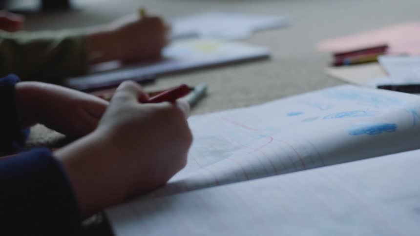 Close up of the hands of a pair of kids drawing with crayons on the bedroom floor