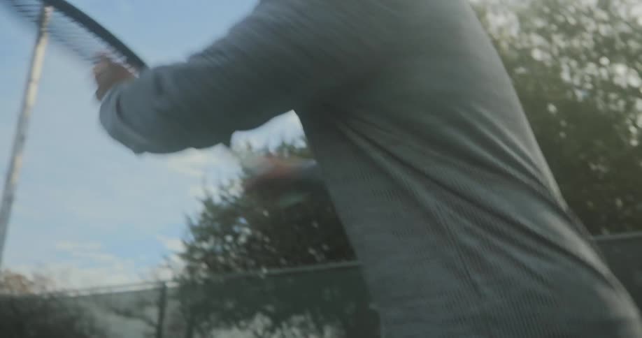 Young vigorous man energetically plays tennis on an outdoors court at morning
