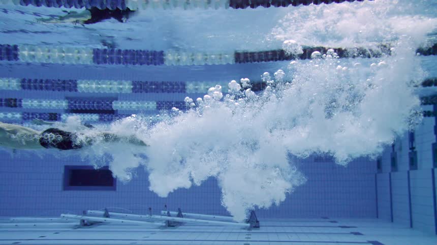 A male and a female diving into a swimming pool and swimming toward end of the pool