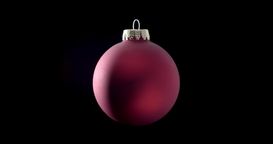 Light shines on a red Christmas ornament as it spins slowly in the darkness