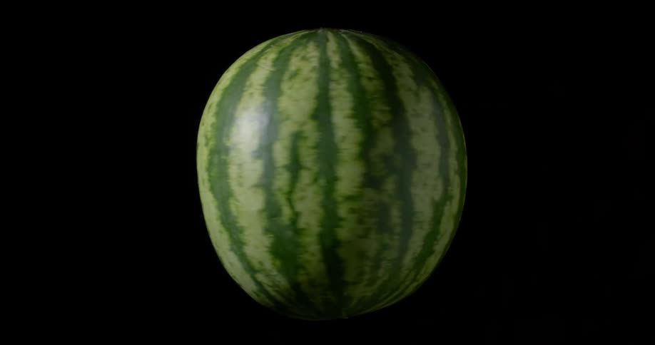 Green organic watermelon spinning around with black background and cinematic lighting in the darkness of a studio
