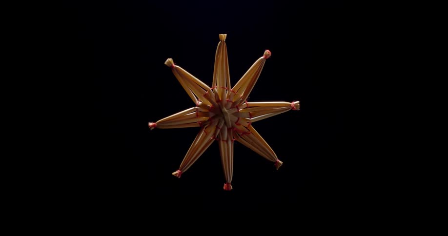 Christmas straw star spinning in front of a black background with an interplay of light and shadow on its surface creating a dynamic visual experience