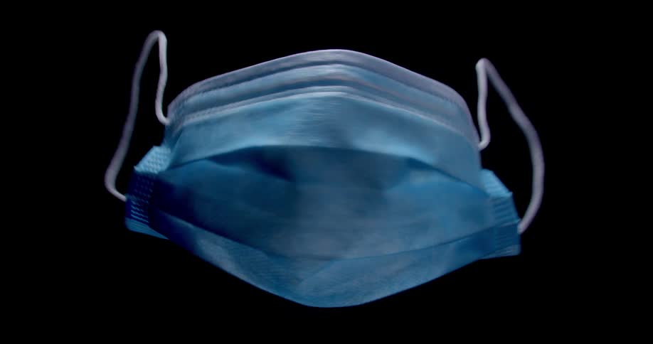 A suspended medical face mask spinning in the air with black background