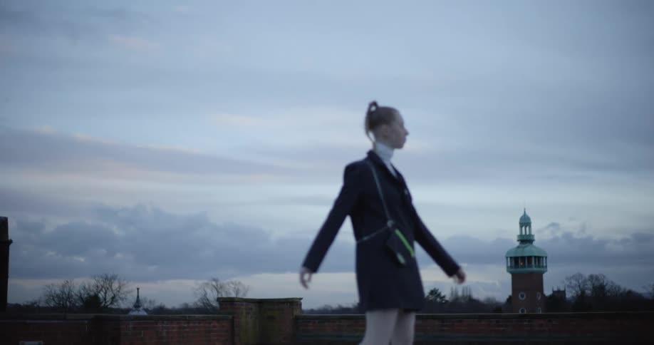 A young woman models for the camera on the roof of an european building at evening