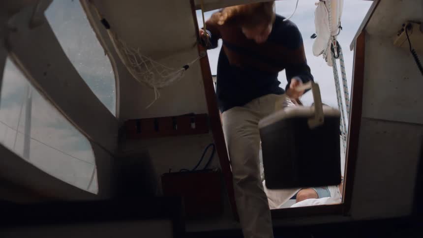 Friends smile as the ones with a fishing pole watch another friend place cooler in boat cabin