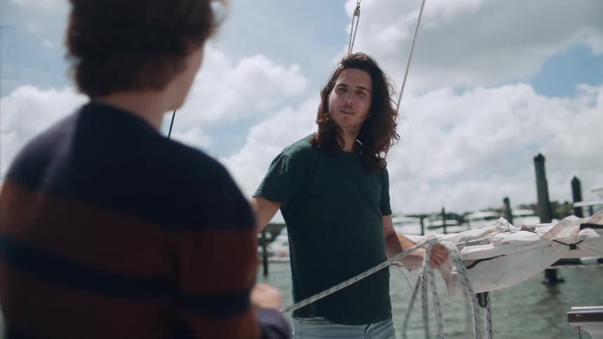 Two men enjoying each others company on a leisurely boating trip with one man coiling up the rope while the other one laughs at his jokes and enjoys the sea breeze