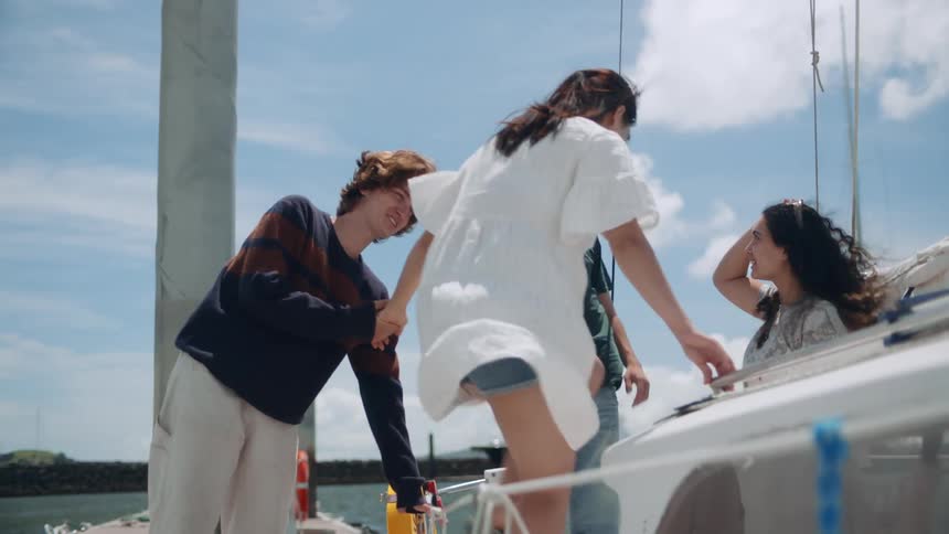 A group of four friends two males and two females are getting off a small boat at the dock with the males holding the females hands and helping them over the side
