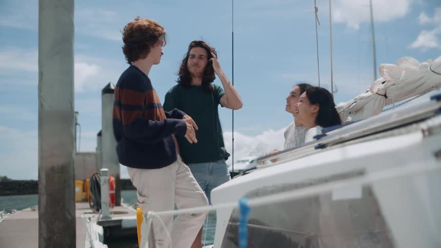 Four young people on a sailboat in the water hanging out and talking