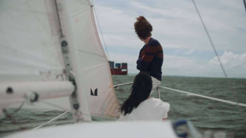 A young man and woman riding on a sailboat on a windy cloudy day