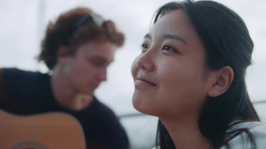 Young girl smiles while listening to a friend playing acoustic guitar on a sailboat
