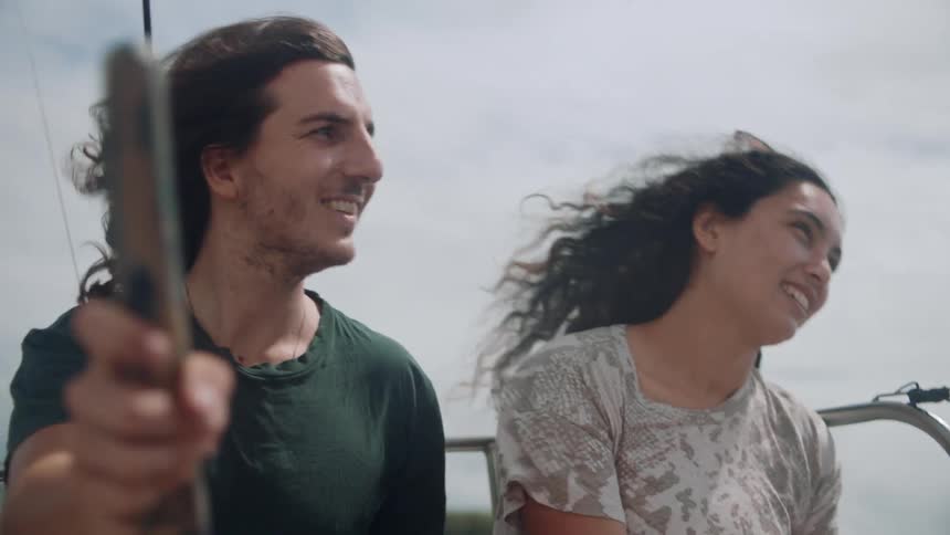 A man and a woman are sitting beside each other smiling with their hair blowing in the wind as the the boat they are in moves up and down with the water