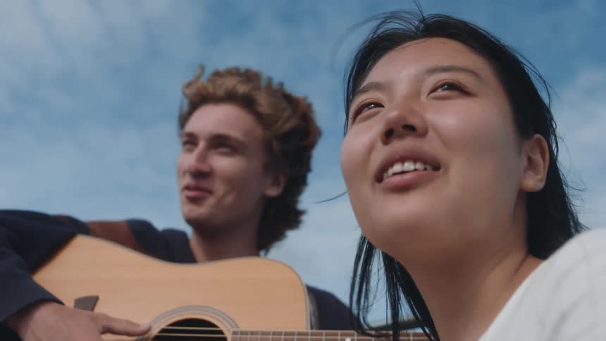 Close up of a happy relaxed couple singing while playing guitar on a sailboat