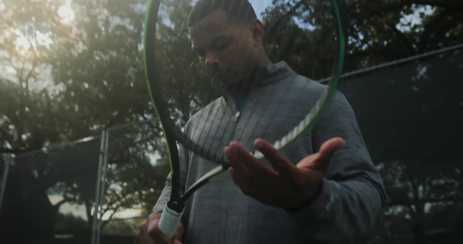 A man spins a tennis racket around while standing on a tennis court