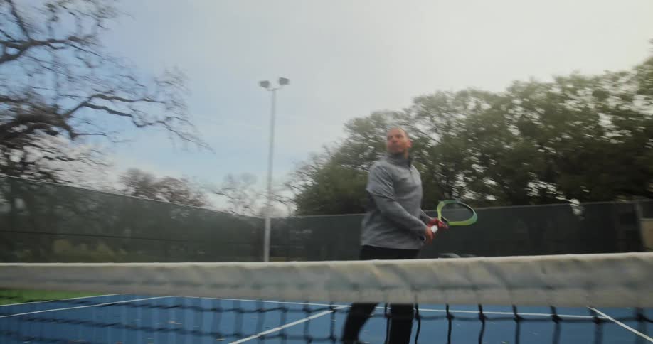 Man with gray shirt black pants plays tennis in the court