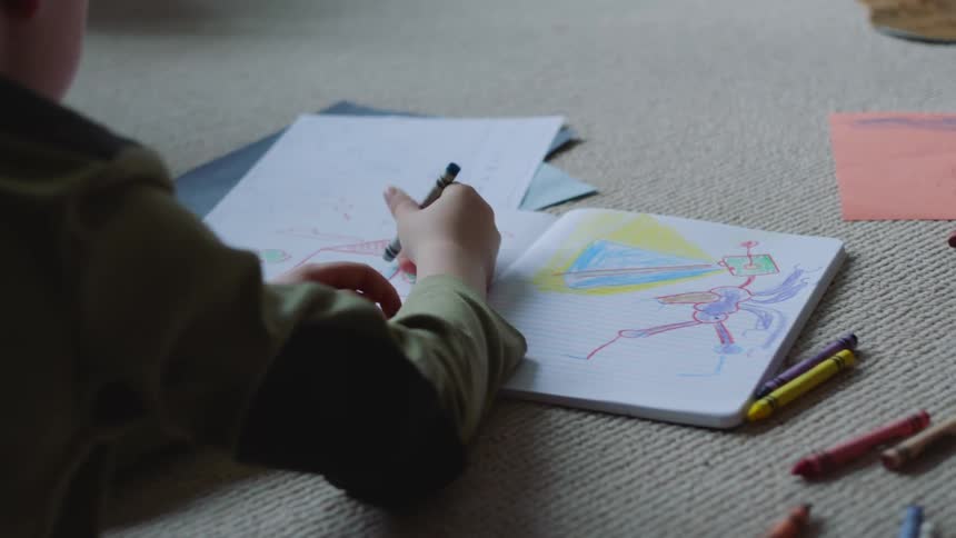Two little boys are sitting on the floor coloring with crayons