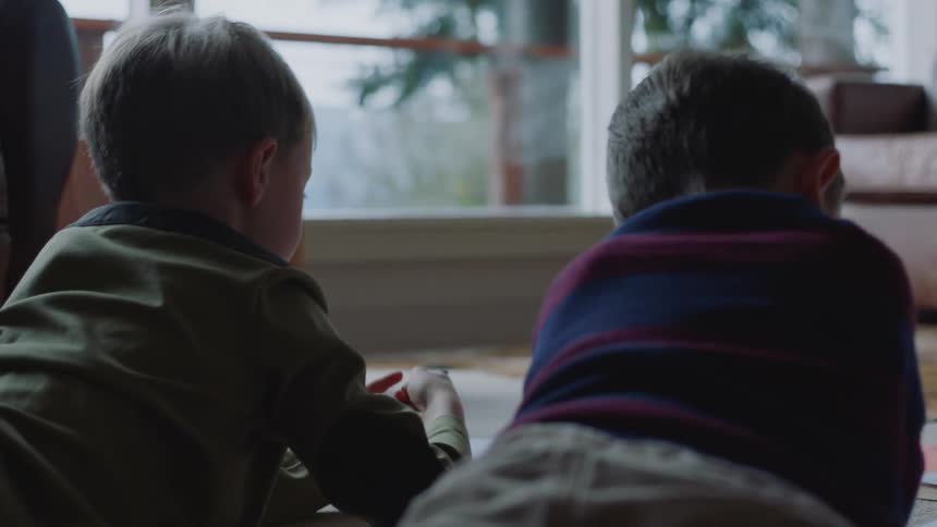 Two little boys are sitting on the floor coloring with crayons