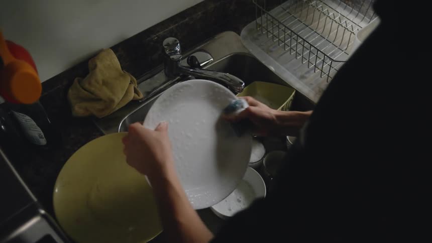 Close up of the hands of a person scrubbing dishes on the kitchen sink at home