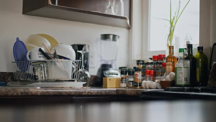 A granite kitchen countertop contains a dish drainer blender and several bottles of spices