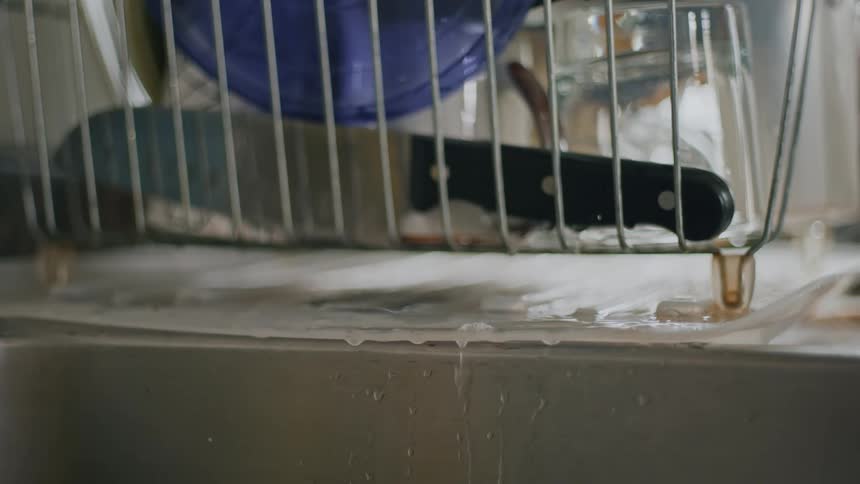 Water drips from a dish drainer into a stainless steel kitchen sink