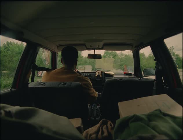 Man inside his car trying to start his car while some boxes and clothes are on the back seat of the car