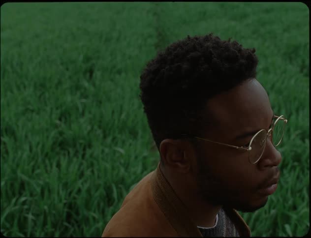 A close up of a mans face putting on glasses with a field of grass in the background