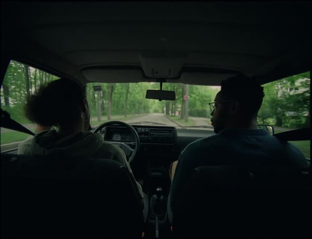 A woman is driving and speaking to the man in the passengers seat beside her who she pushes away when he tries to hold her hand and she places her head on her other hand in frustration while he remains looking forward