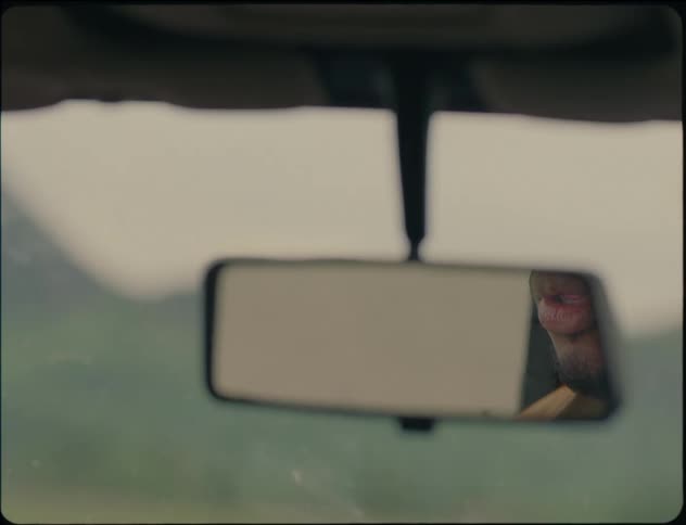 A man reflected in a car rear view mirror