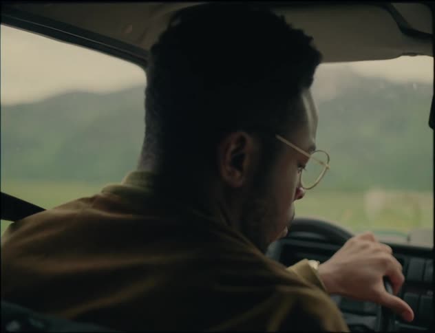 Man with glasses beard and brown jacket drives car in the country