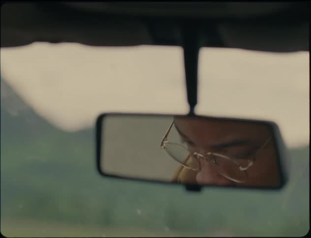 A man sitting in his car and looking at himself in the rearview mirror he is as well putting on a pair of glasses