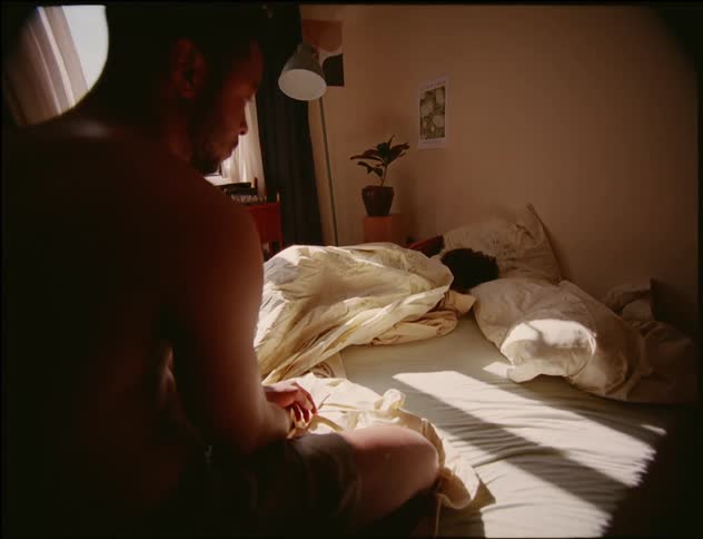 Man sits on bed while woman shifts under covers