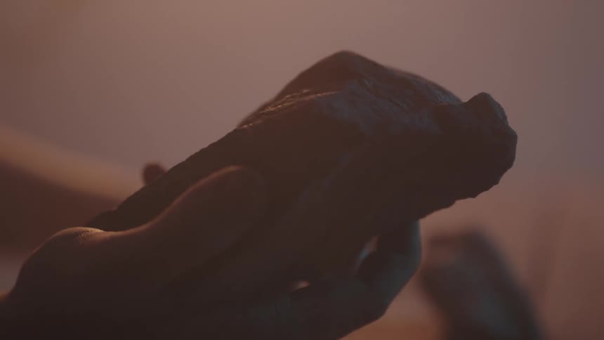 A hand lifts a rock and turns it as if examining it
