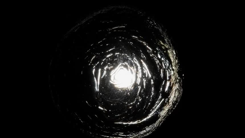 A circle of water against a black background ripples and has a light in the center of it