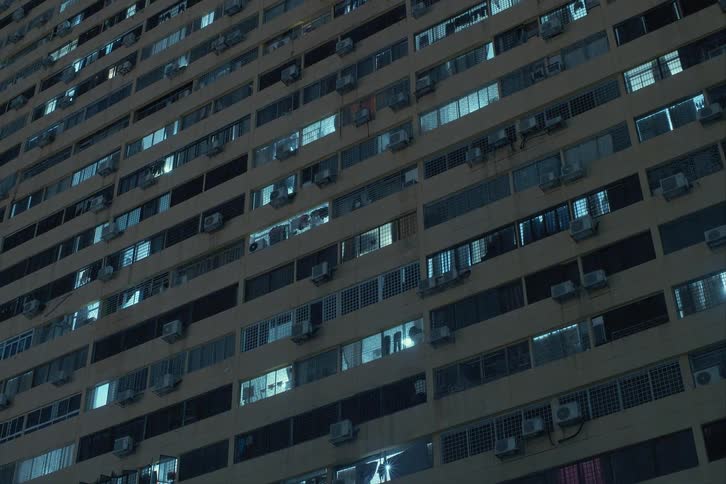 Apartment lights shine from ac unit dotted building as night falls
