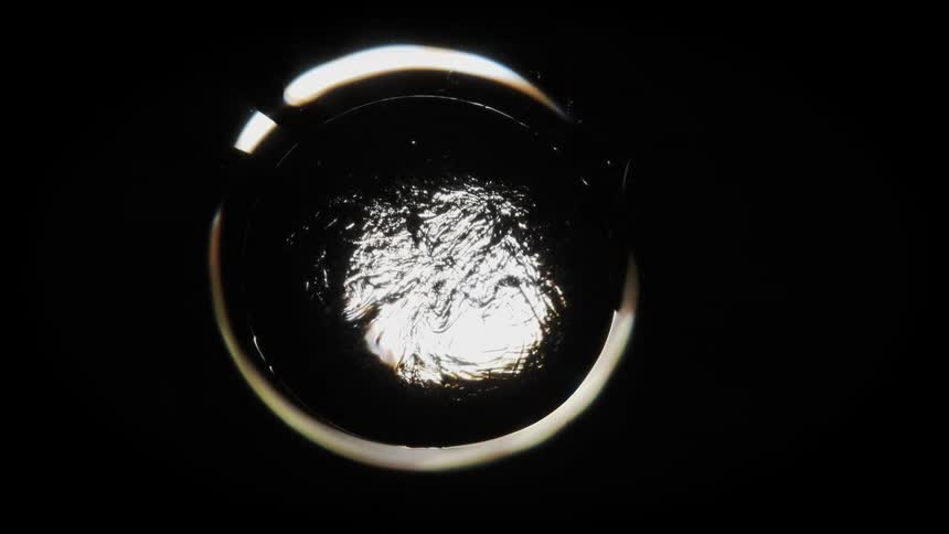 Top down close up view of a thick black liquid bubbling up reflecting light