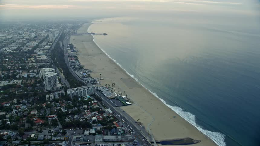 Aerial footage captures the California sunrise over a residential area leading towards the sea showcasing Santa Monica Pier and its surrounding beaches and coastline