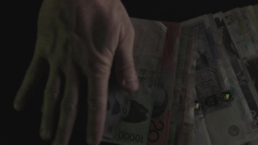 A hand spreads out several paper bills of a foreign currency