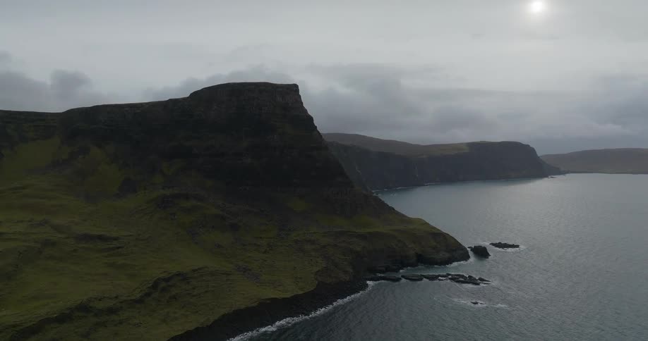Aerial view of a tall mountain towering over the coast close to the cliffs on an overcast day