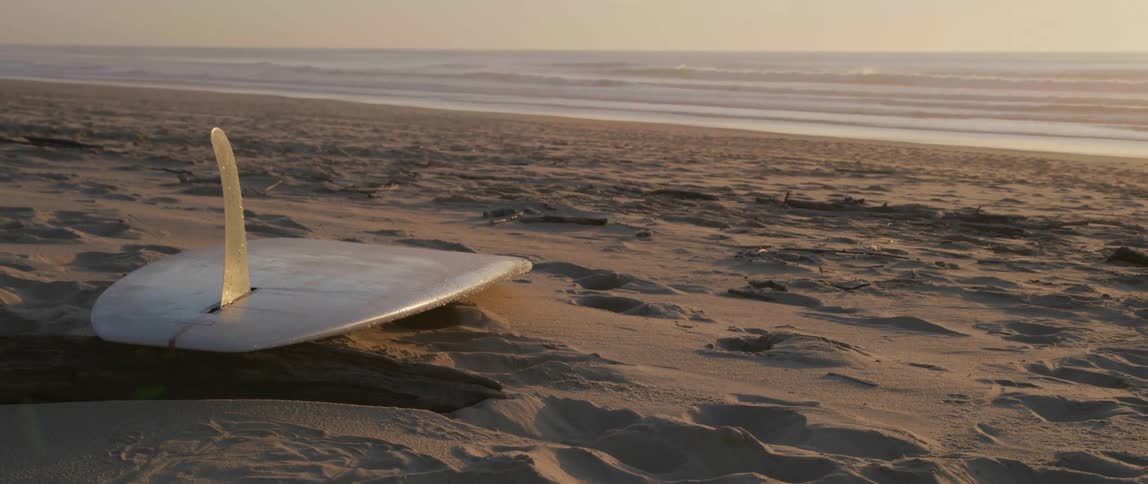 A surfboard is lying on the sand on the beach as waves roll in to shore
