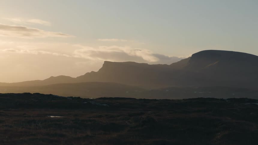 A silhouette of a mountain range in the distance against a slightly cloudy sky